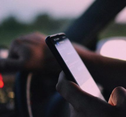 Close-up of a person using a smartphone while driving in a car at dusk.